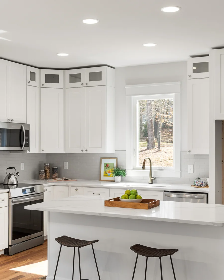 Warm white kitchen with pale stone island, light wood stools and natural daylight